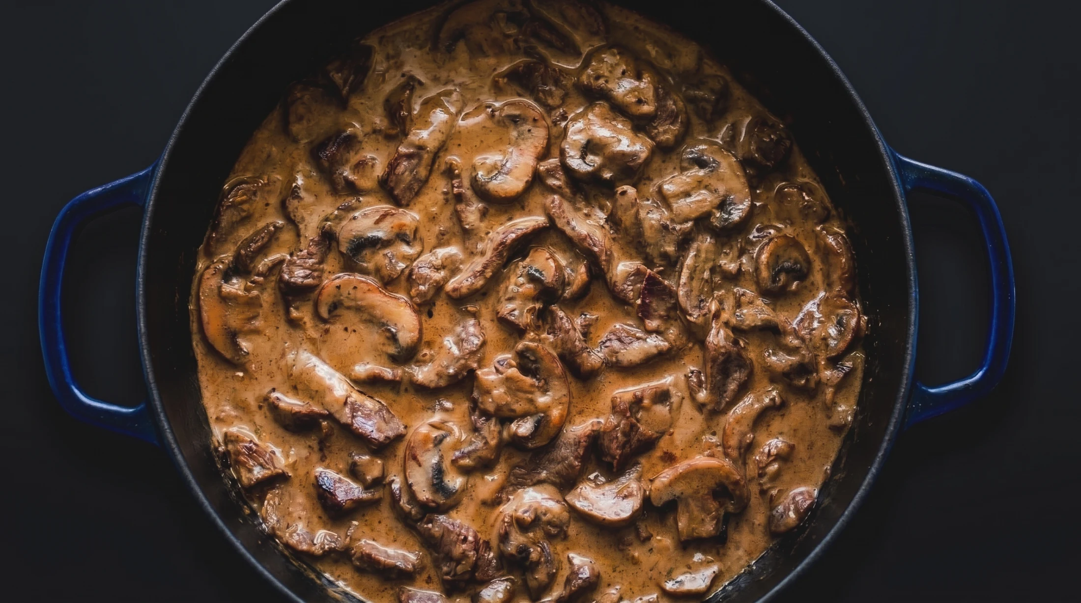 Beef stroganoff with sliced mushrooms in a blue Dutch oven