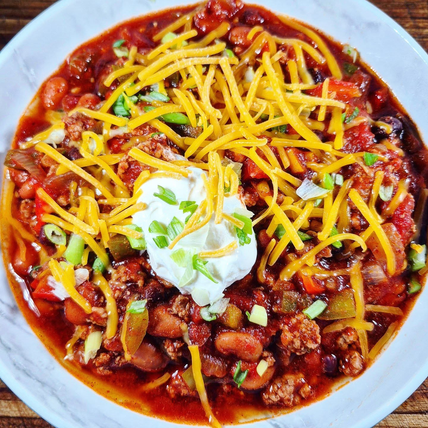Slow cooker chili with fresh tomatoes, beans, ground meat, shredded cheddar, sour cream, and green onions