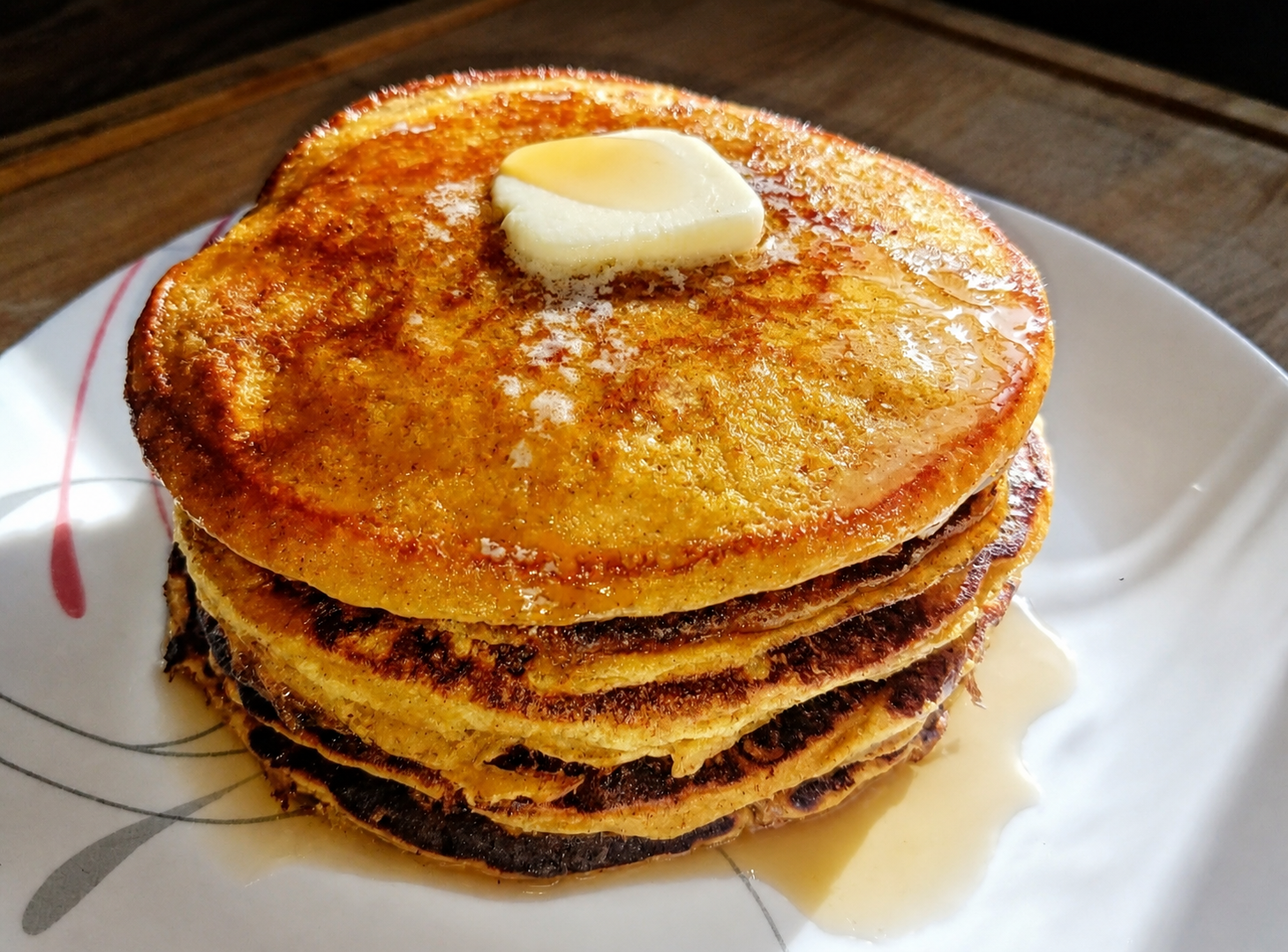 A warm stack of golden pumpkin pancakes with butter and syrup